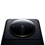 Close-up of a black device with a large circular camera module and glossy lens surrounded by rings, resting on a textured surface